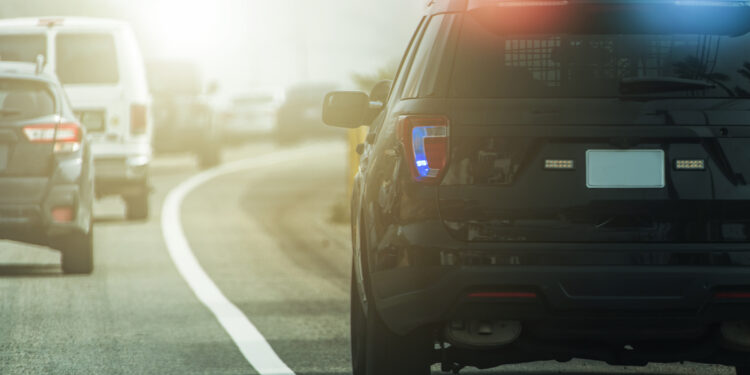 Flashing Lights of American Modern Highway Police Patrol Cruiser on Side of a Road. Rear View. Transportation and Police Enforcement Theme.