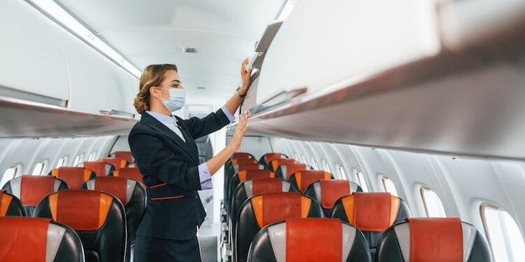 In mask. Young stewardess on the work in the passanger airplane.