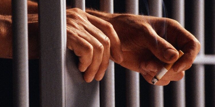 Prisoner Holding Cigarette Between Bars