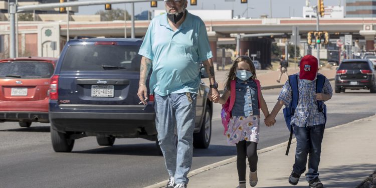 Pedestrians walk along a sidewalk as cars pass by on San Pedro Avenue on Wednesday.